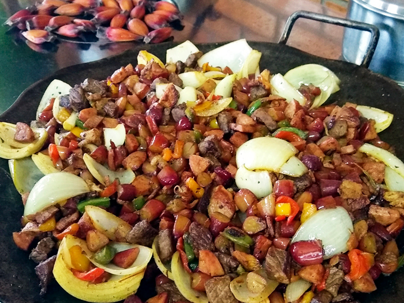 na imagem, vemos um prato sobreposto a outro. Ambos possuem detalhes floridos, em tons azuis e rosa. Dentro do prato que está acima, temos uma mistura que leva diversas carnes picadas: de gado, linguiça e outras, além de pinhões e afins.