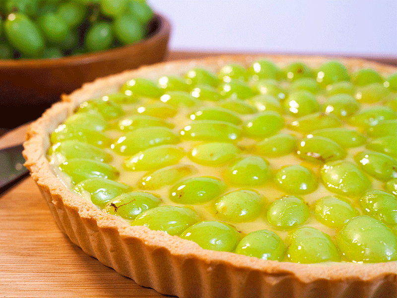 Sobre uma superfície de madeira, há uma torta com uvas de cor verde.