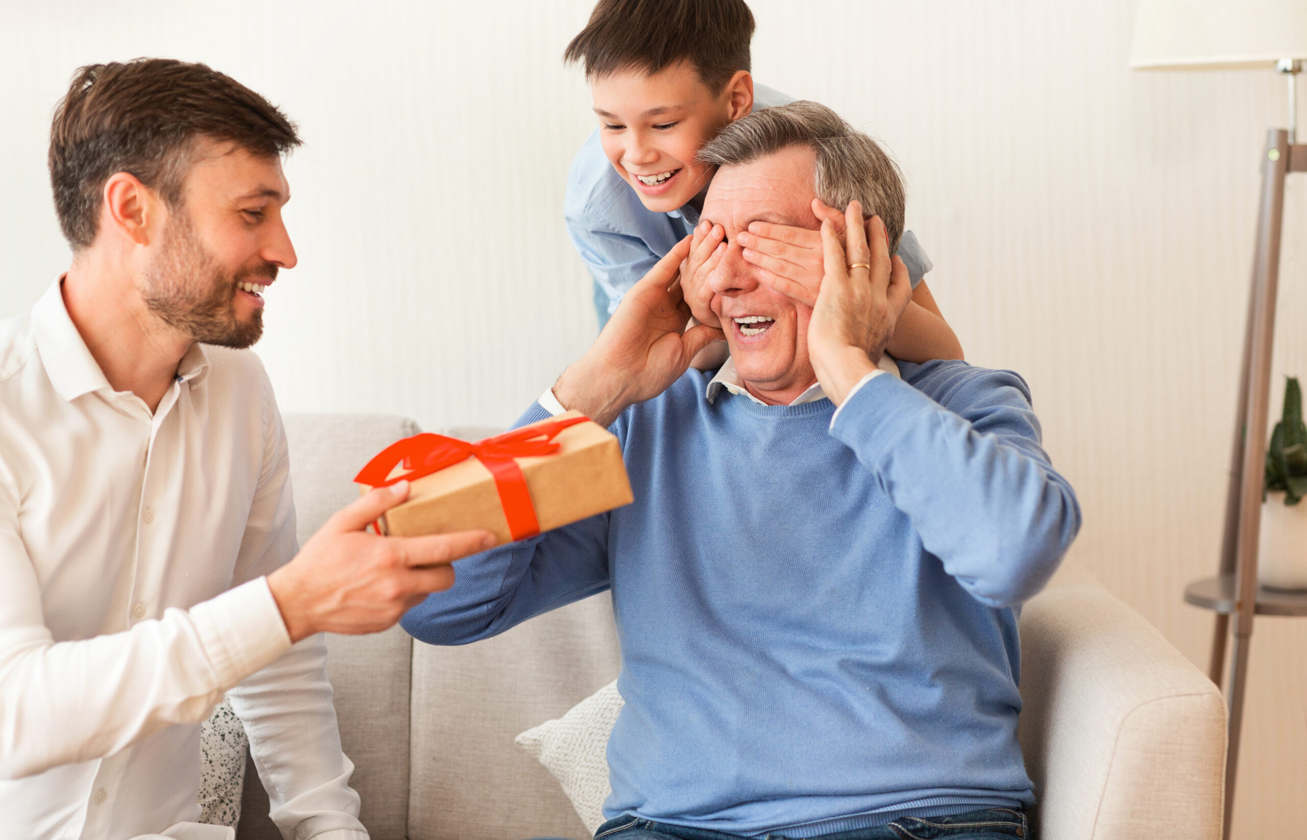 Pai recebe presente do filho enquanto o neto cobre seus olhos, em momento de carinho no Dia dos Pais.